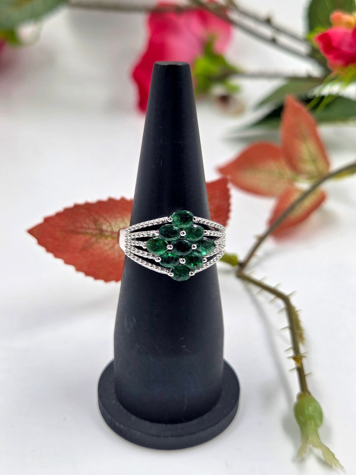 Sterling silver emerald ring on display stand with oval cluster of green stones